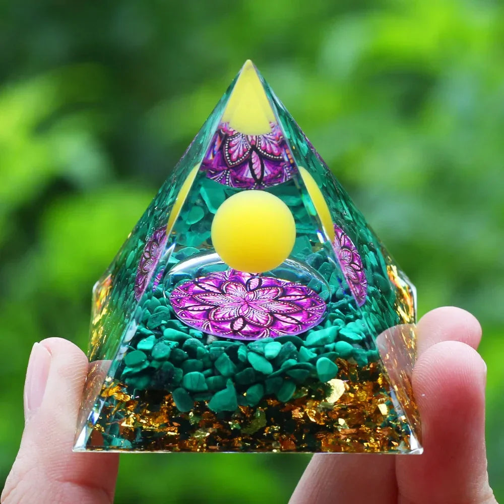 Triangular crystal with yellow balls and purple floral designs held in a hand against a green blurred background