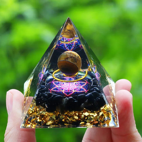 Pyramid-shaped crystal with intricate designs held by a hand against a green blurred background