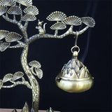 Decorative incense burner hanging from a tree branch with a dark background