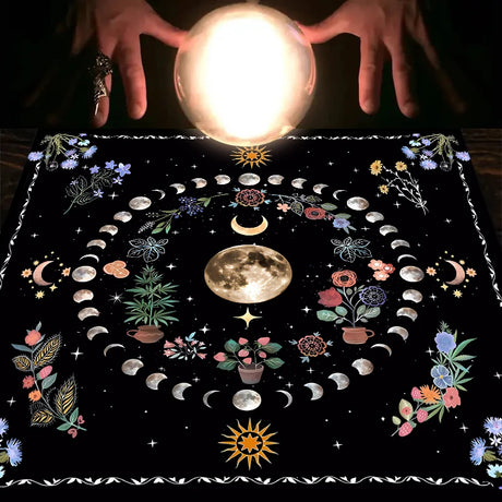 Crystal ball held above a black cloth with astrological designs and plants.