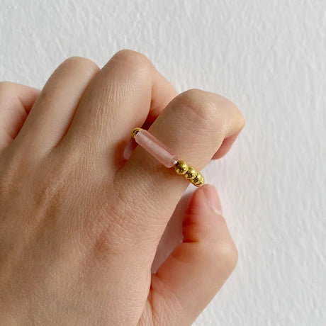 Hand wearing a gold beaded ring on a plain background