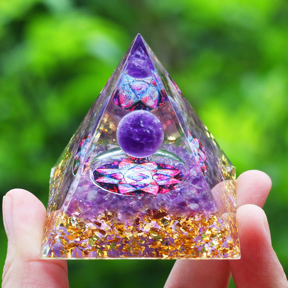 Pyramid-shaped crystal with purple ball and colorful interior held by a hand against a green blurred background