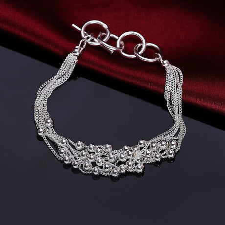 Silver bracelet with chain and bead details on a dark surface with red fabric background