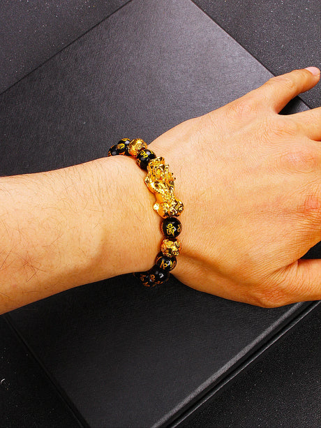 Hand wearing a black and gold beaded bracelet on a dark surface