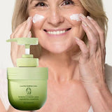 Woman applying cream to her face with a green skincare product in the foreground.