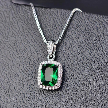 Green gemstone pendant with silver chain on a textured gray background