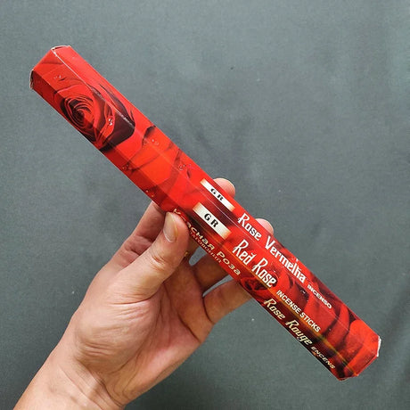 Hand holding a red incense stick box with 'Red Rose' branding against a gray background