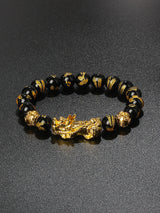 Black beaded bracelet with gold accents and a large gold dragon charm on a dark background