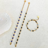 Gold necklace and bracelet with blue and black beads on a textured white surface