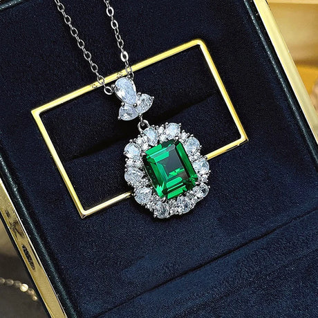 Green gemstone pendant with diamond accents on a chain, displayed on a dark blue cushion.
