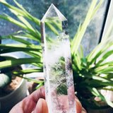 Clear crystal held by a hand with green plants in the background