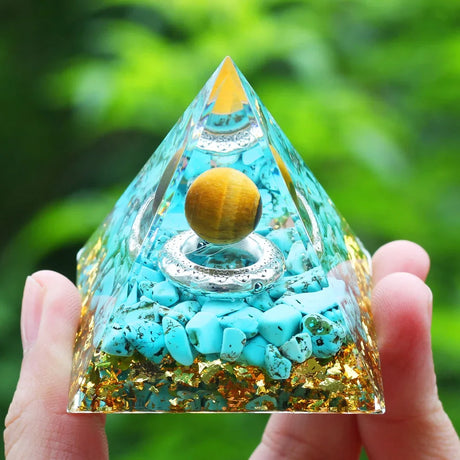 Pyramid-shaped crystal with turquoise stones and a yellow sphere, held in hand with green blurred background