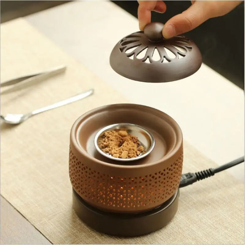 Ceramic incense burner with a hand holding the lid on a table.