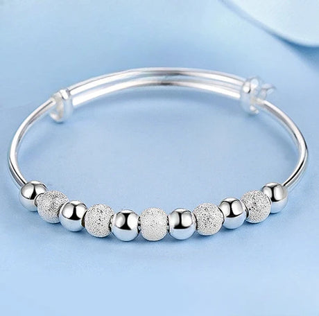 Silver bracelet with textured beads on a light blue background