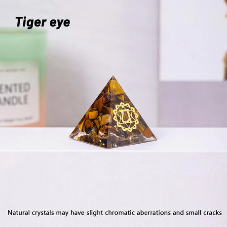Tiger eye pyramid crystal with a gold emblem on a white surface