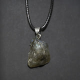 Raw diamond pendant on a chain against a dark background