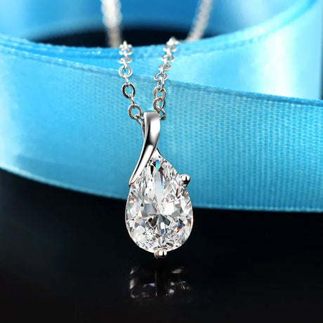 Teardrop-shaped diamond pendant on a chain against a blue ribbon background