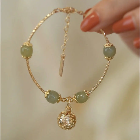 Gold bracelet with green beads held by a hand against a neutral background
