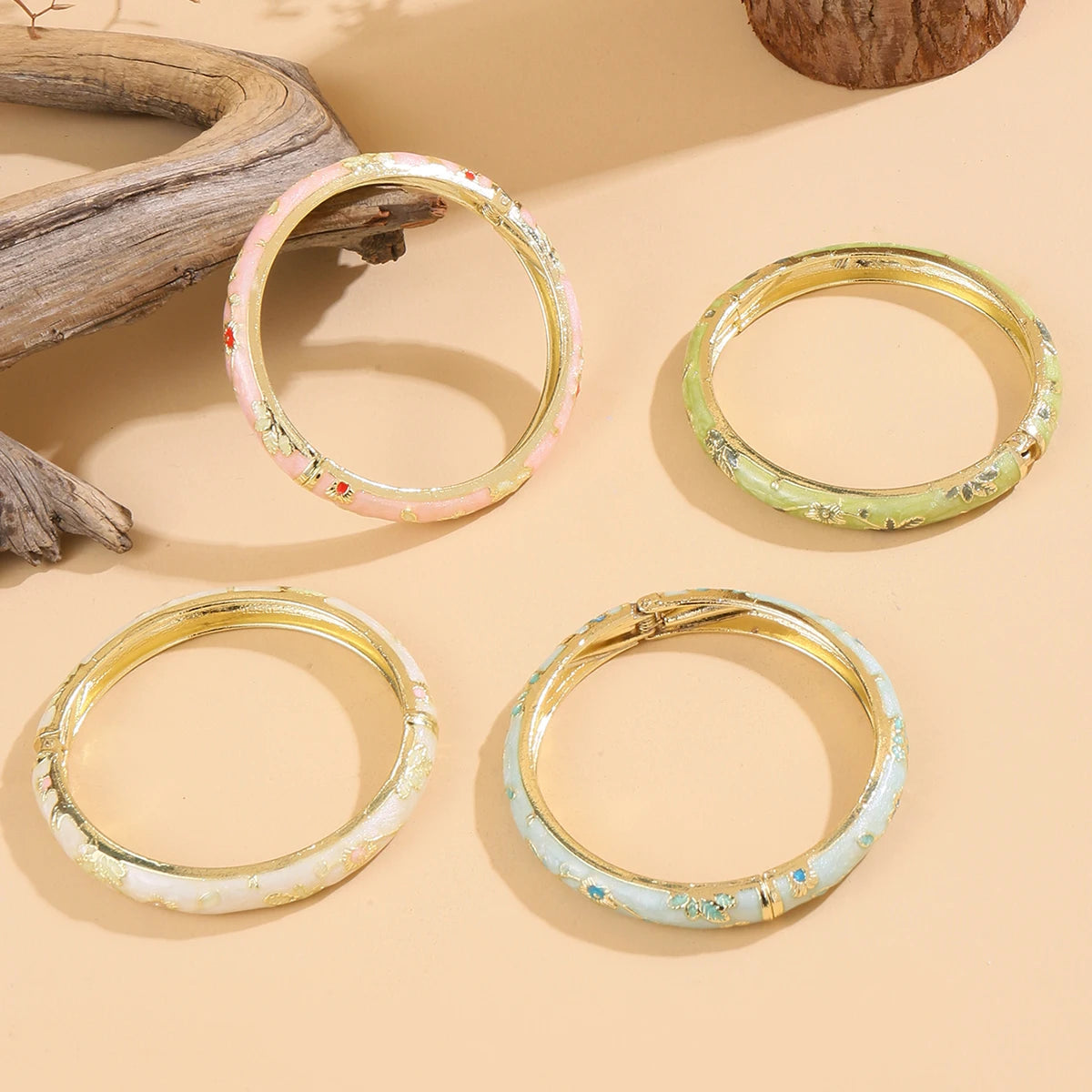 Four gold-rimmed bangles with colorful interior patterns on a beige surface.