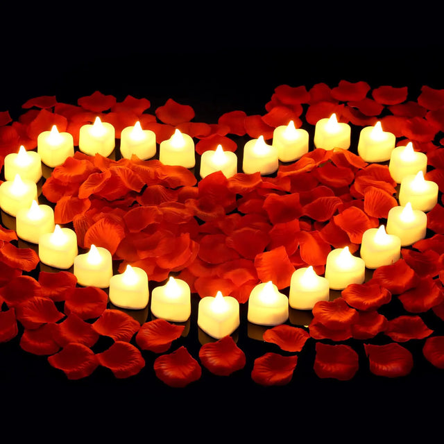 Heart shape made of red rose petals and white candles on a black background