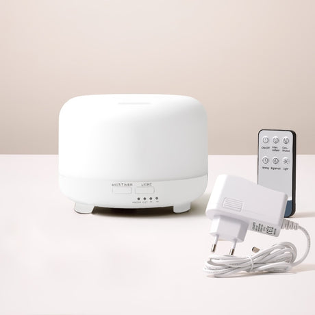White essential oil diffuser with remote control and power adapter on a light beige background