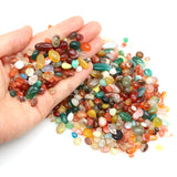 Hand holding a variety of small, multicolored stones on a white background