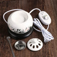 White ceramic warmer with control panel, lid, and spoon on a wooden surface
