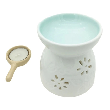 White ceramic oil burner with floral designs and a small candle on a white background