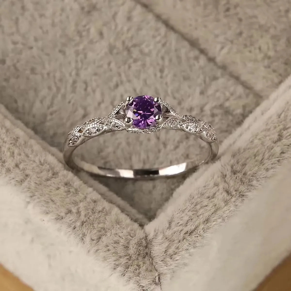 Silver ring with a purple gemstone in a soft fabric box