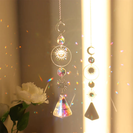 Decorative hanging crystal with sun, moon, and star designs in front of a light curtain.