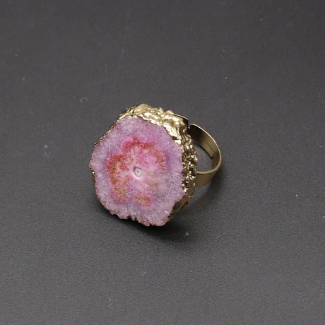 Ring with pink geode-like stone and gold band on a dark gray background
