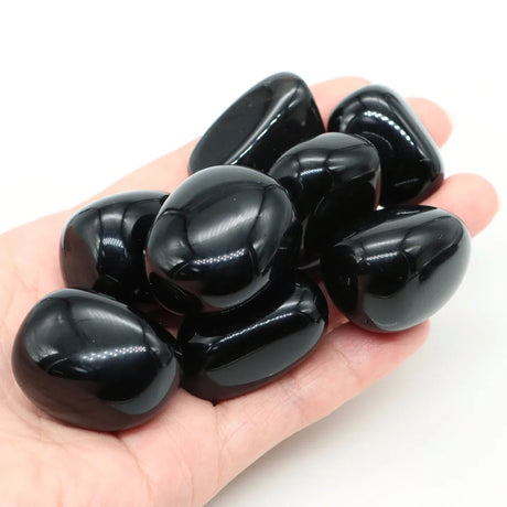 Hand holding a pile of glossy black stones on a white background