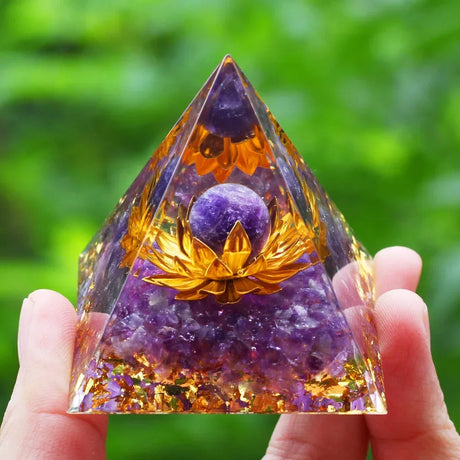 Pyramid-shaped crystal with purple and orange colors held by a hand against a green blurred background