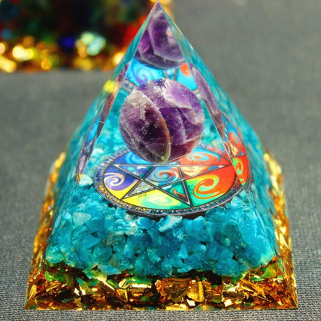Pyramid-shaped crystal with colorful interior and gold base on a gray surface