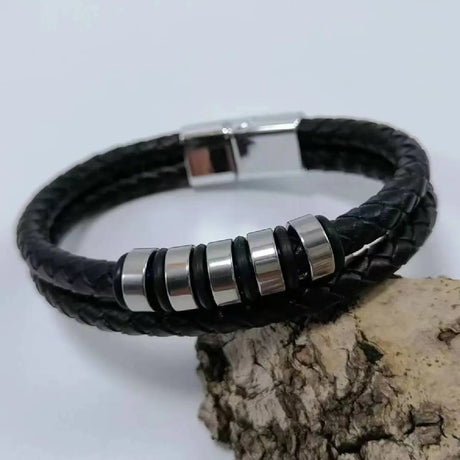 Black braided leather bracelet with silver cylindrical beads on a light gray background