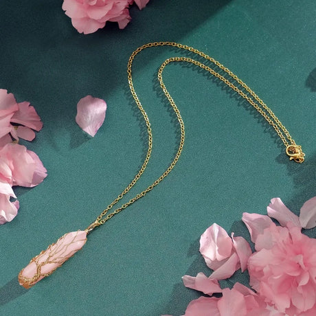 Gold necklace with a pink pendant on a green background with pink flowers