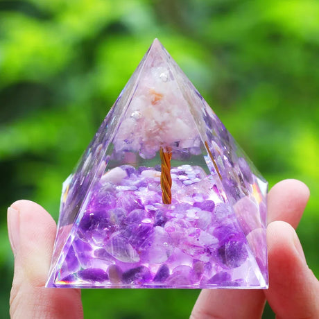 Pyramid-shaped crystal with purple and clear stones held by a hand against a green blurred background