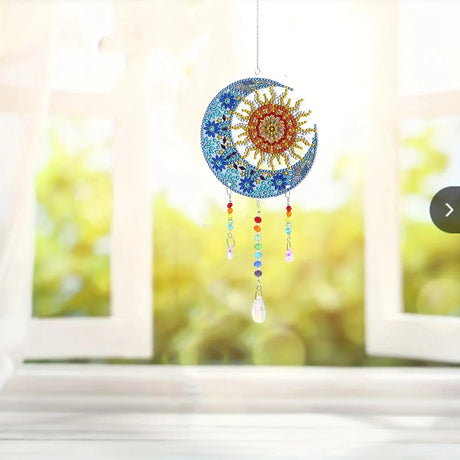 Decorative sun and moon ornament with colorful beads hanging in front of a window with greenery.