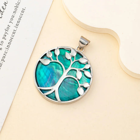 Tree-shaped pendant with turquoise center and silver border on a beige surface