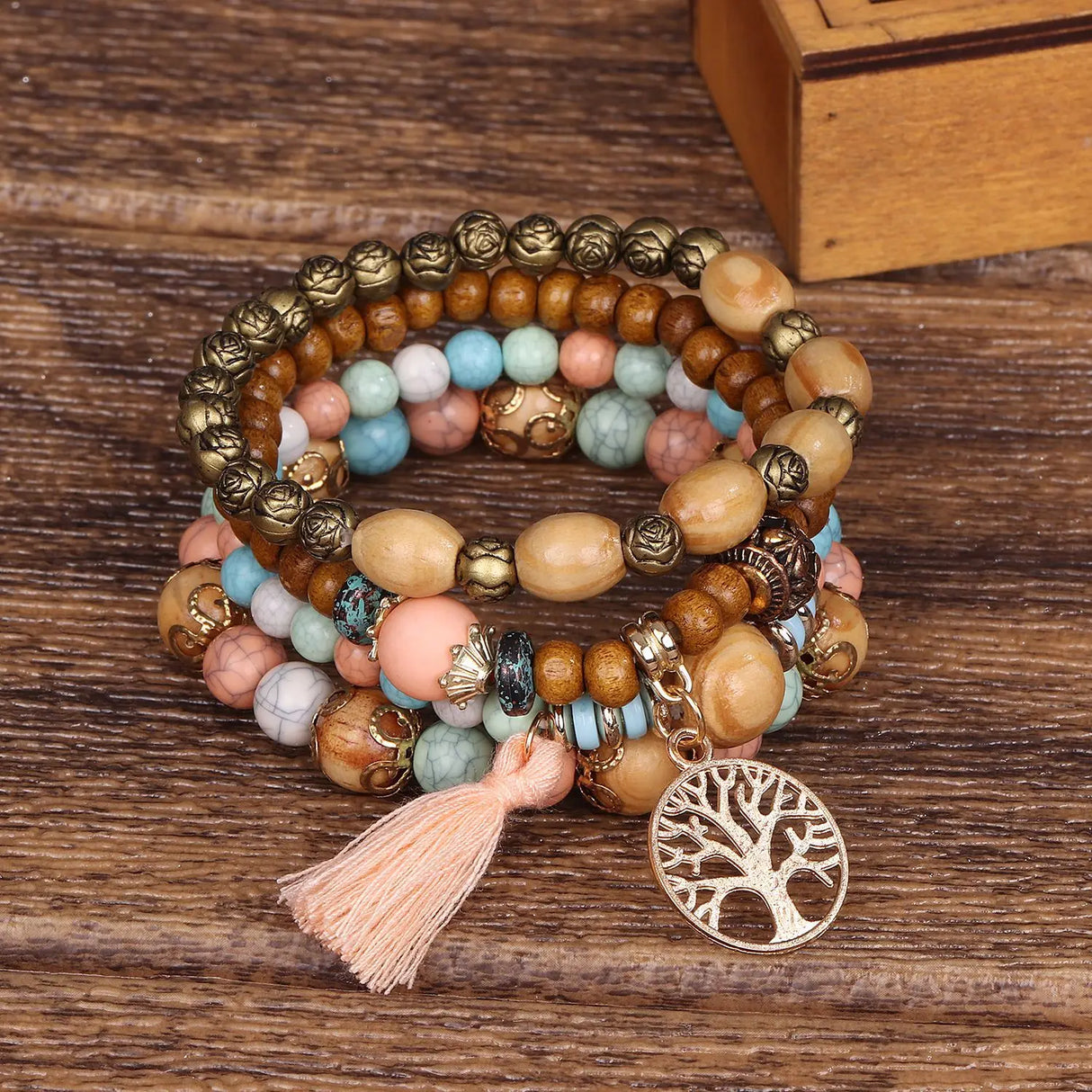 Multicolored beaded bracelet with tassel and tree of life charm on a wooden surface