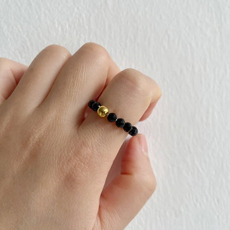 Hand wearing a black beaded ring with a gold accent on a white background