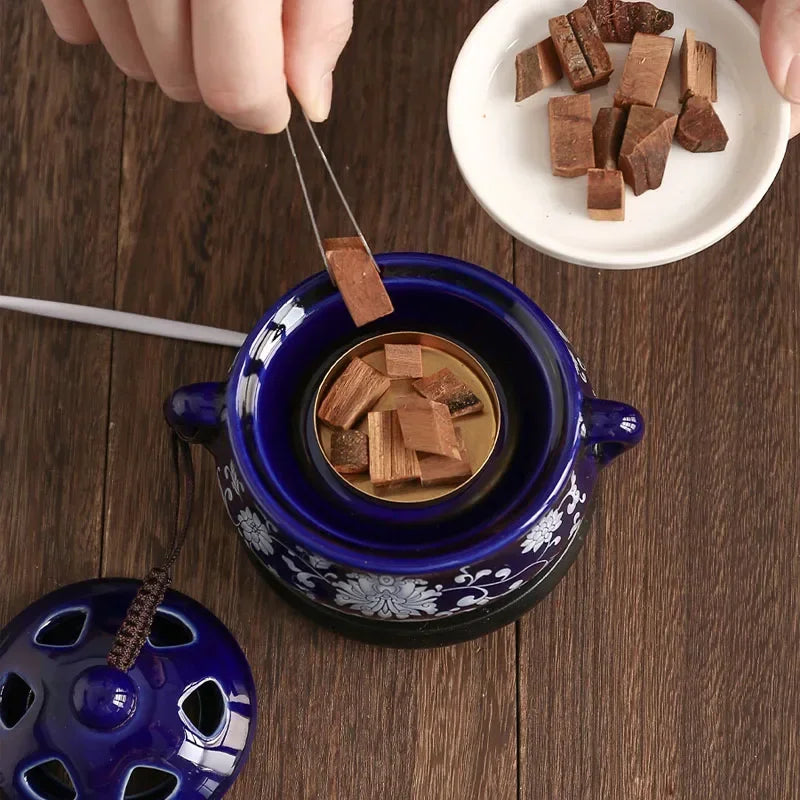 Blue ceramic warmer with wooden pieces being added on a wooden surface