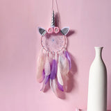 Unicorn-themed dreamcatcher with feathers on a pink wall next to a white vase.