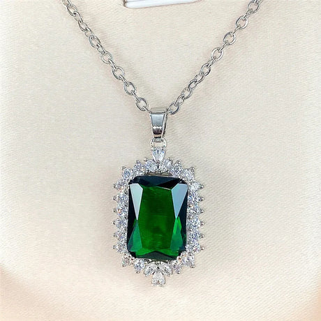 Green gemstone pendant with diamond accents on a silver chain against a beige background