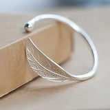 Silver feather-shaped bangle on a beige background