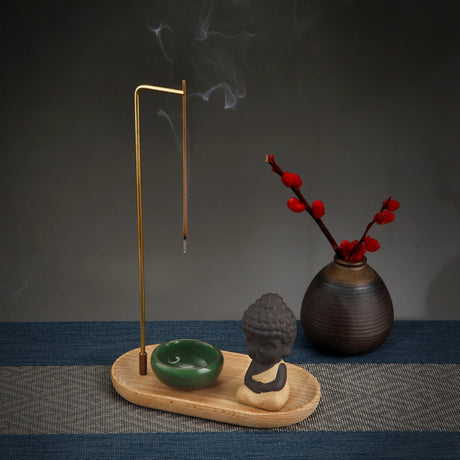 Incense burner with incense stick, small Buddha statue, and vase with red flowers on a textured surface.