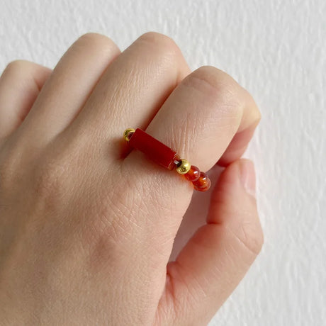 Hand wearing a red beaded ring with gold accents on a white background