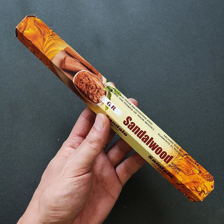 Hand holding a sandalwood incense stick with a dark gray background