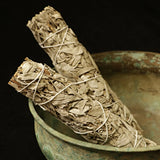 Two bundles of sage wrapped with twine on a textured surface