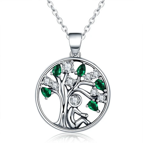 Silver tree of life pendant with green and clear gemstones on a white background